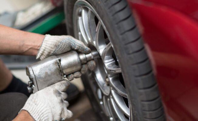 Dekkskift hos Mekonomen, mekaniker skrur til julbolter på rød bil.