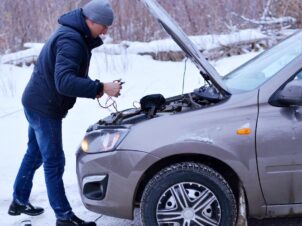 Mørkkledd mann med lue forsøker å starte en vinterkald grå bil