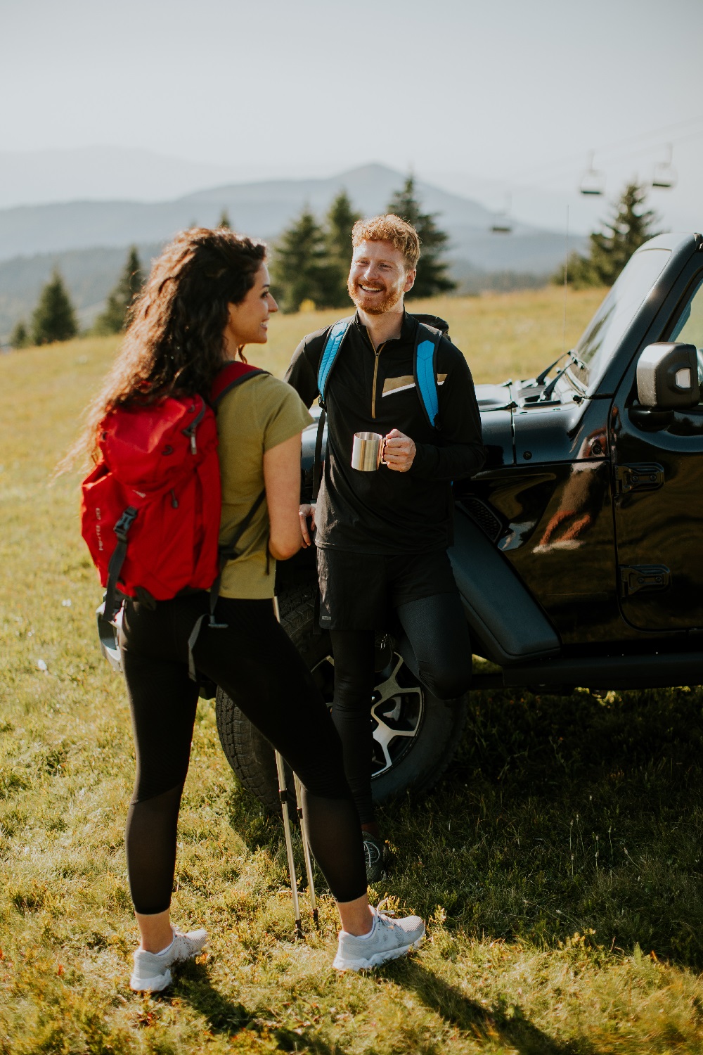 Ungt par på fjelltur nyter kaffepause ved en svart Jeep