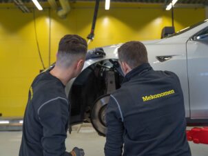 To mekanikere sjekker bremsene på hvit bil inne på mverkstede ded gule vegger