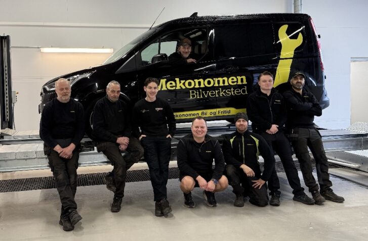 Åtte mekanikere foran svart Mekonomen bil inne på verkstedet