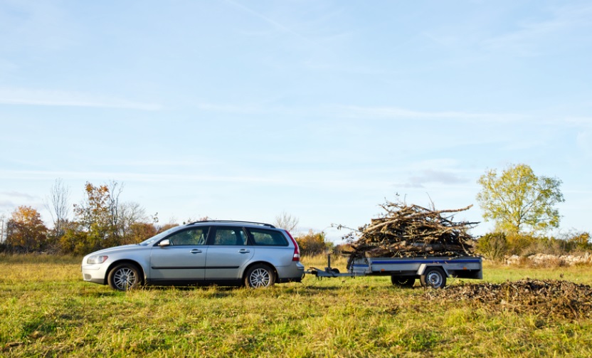 Sølvgrå stasjonsvogn kjører høstløv i tilhengeren