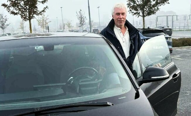 Mann står med åpen dør på sin svarte BMW I3 på en parkeringsplass en gråværsdag