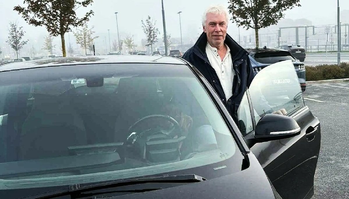 Mann står med åpen dør på sin svarte BMW I3 på en parkeringsplass en gråværsdag