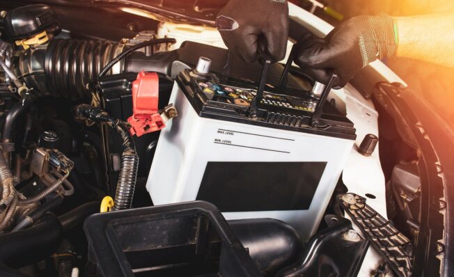 Mekanikerens hender tar ut ett hvitt bilbatteri for å bytte